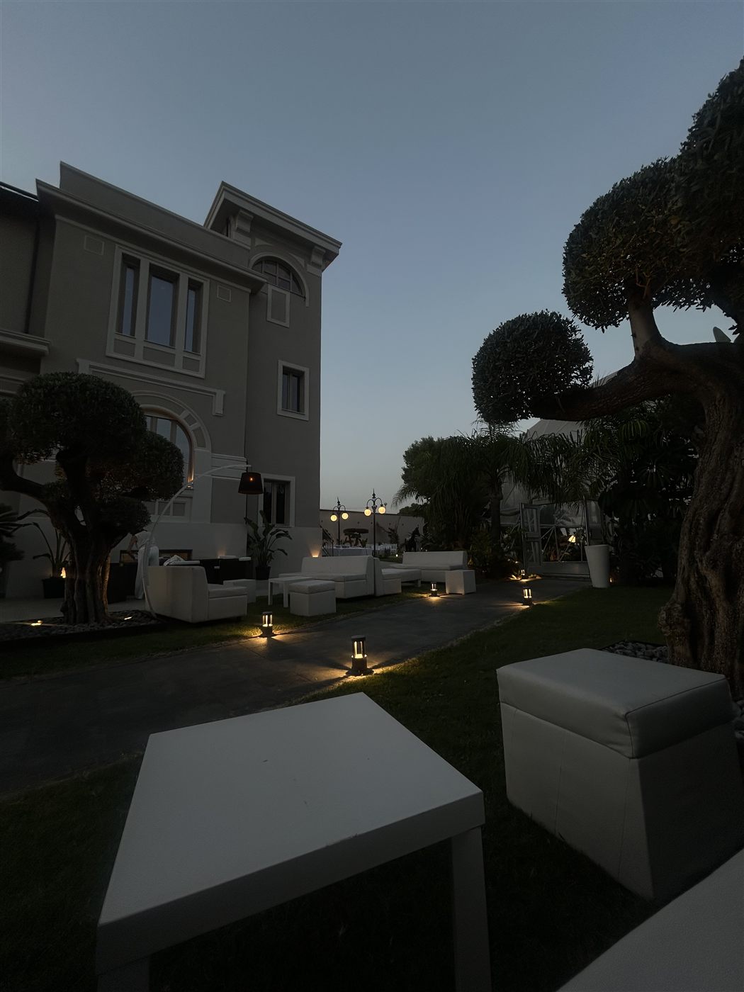 Area lounge del giardino di Villa CaStè al tramonto, tra ulivi secolari e sedute bianche