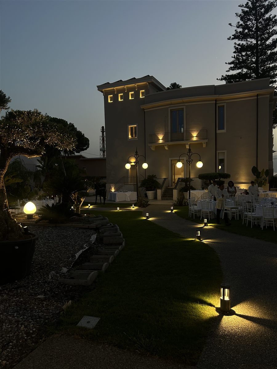 Facciata illuminata della villa vista dal giardino con tavoli imbanditi per un evento